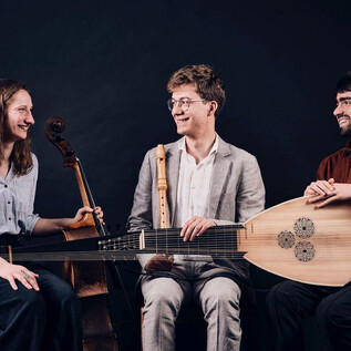 Trzech muzyków siedzi razem i gra na różnych instrumentach. Uśmiechają się i cieszą atmosferą. | © Johannes Berger