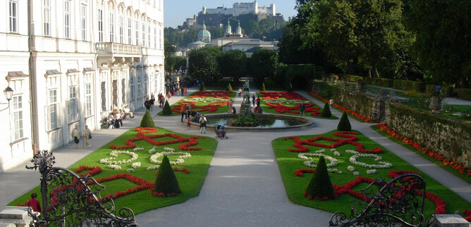 A beautiful garden with colorful flower beds and a fountain. In the background, a historical castle can be seen. | © Tourismus Salzburg