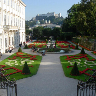 A beautiful garden with colorful flower beds and a fountain. In the background, a historical castle can be seen. | © Tourismus Salzburg