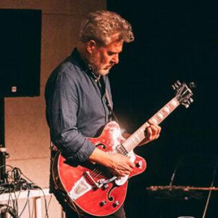 A musician passionately plays guitar on stage. In the background, technical equipment and a microphone can be seen. | © Jahvo Joža