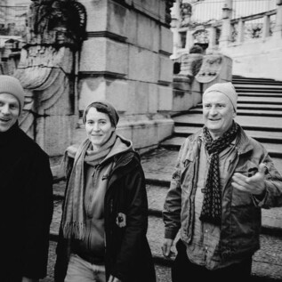 Trzej ludzie radośnie schodzą po schodach. Noszą wygodne ubrania i czapki w miejskim otoczeniu. | © Eckhard Derschmidt