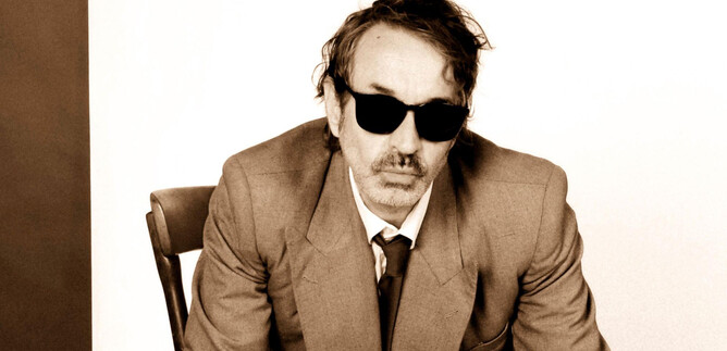 A man in a suit is sitting in a chair and wearing sunglasses. The background is neutral and enhances his appearance. | © Michelle Rassnitzer