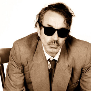 A man in a suit is sitting in a chair and wearing sunglasses. The background is neutral and enhances his appearance. | © Michelle Rassnitzer