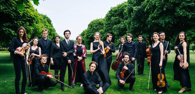 A group of musicians is standing outdoors on a green meadow. They are wearing elegant black clothing and holding various instruments in their hands. | © Freie Kunst