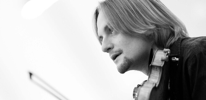 Un musicista suona il violino e ha i capelli lunghi. La ripresa è in bianco e nero. | © DomRadio