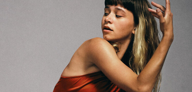 Eine Frau in einem roten Kleid posiert künstlerisch. Sie hat lange, gewellte Haare und einen ausdrucksvollen Blick. | © Chris Rogl