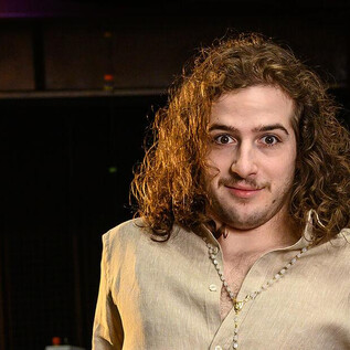 Egy fiatalember göndör hajjal áll egy szobában. Egyszerű felsőt visel, és közvetlenül a kamerába néz. | © SLT / Tobias Witzgall