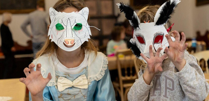 Due bambini indossano maschere di animali colorate e posano in modo giocoso. Sembriamo divertirci in una stanza festosa. | © DomQuartier