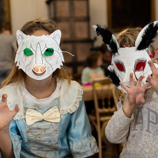 Two children are wearing colorful animal masks and are playfully posing. They seem to be having fun in a festive room. | © DomQuartier