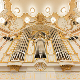 Un grand orgue majestueux avec de nombreuses tuyaux dans une salle décorée de façon festive. Les murs sont peints dans des couleurs douces et ornés de détails dorés. | © Wolfgang Lienbacher