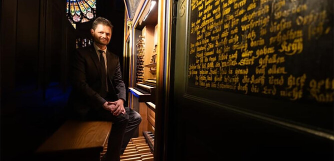Un uomo è seduto in una stanza storica con un organo. Sullo sfondo si possono vedere finestre colorate e scritte dorate sulla parete. | © Jérôme Dorkel - Ville de Strasbourg