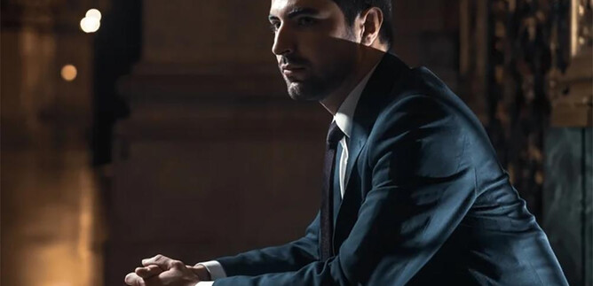 Un uomo pensieroso in un elegante completo è seduto in un luogo stiloso. La luce crea un'atmosfera particolare sullo sfondo. | © James Orford