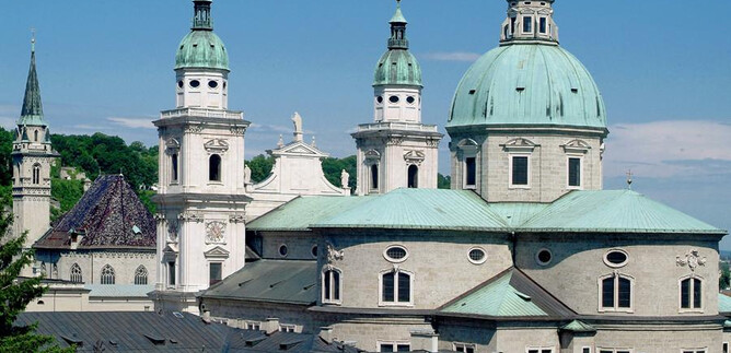 An impressive church architecture with green domes and tall towers. The clear sky complements the historical beauty of the building. | © Erzdiözse Salzburg, Foto: J. Kral