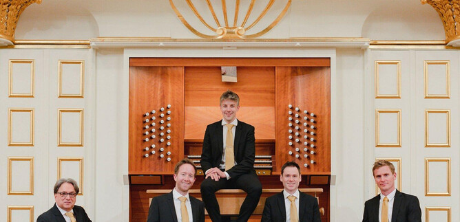A group of five musicians stands and sits in front of an organ. They wear elegant suits and smile at the camera. | © Sophie Baubin
