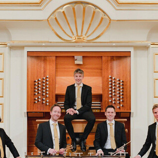 Un groupe de cinq musiciens se tient et s'assoit devant un orgue. Ils portent des costumes élégants et sourient à la caméra. | © Sophie Baubin