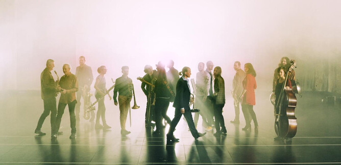A group of musicians stands in a moody fog. They play various wind instruments, and a double bass figure is also visible. | © Lukas Beck