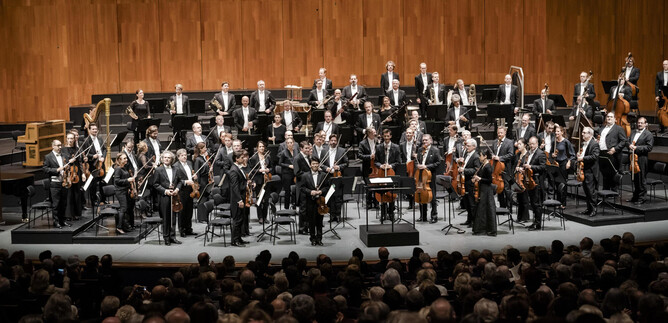 Una gran orquesta está en el escenario y toca un concierto. En el público se pueden ver muchos oyentes. | © Stephan Rabold