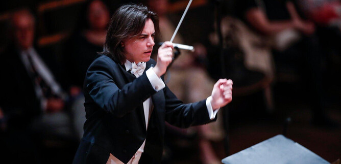 A conductor leads an orchestra on stage. The audience in the background is attentive and enjoying the performance. | © Salzburger Kulturvereinigung_Pixell