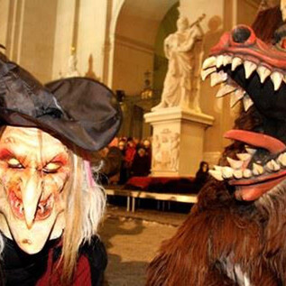 Two figures in costumes stand next to each other: a witch with a spooky mask and a furry creature with sharp teeth. The atmosphere is festive and mysterious. | © Foto: www.christkindlmarkt.co.at, Salzburg