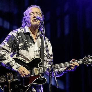 Ein Musiker steht auf der Bühne und spielt Gitarre. Er trägt ein auffälliges Hemd und singt in ein Mikrofon. | © Alexander Müller