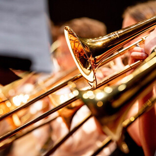 Grupa puzonistów z błyszczącymi instrumentami. Fokus jest na puzonach i muzykach w tle. | © Salzburger Kulturvereinigung_shutterstock
