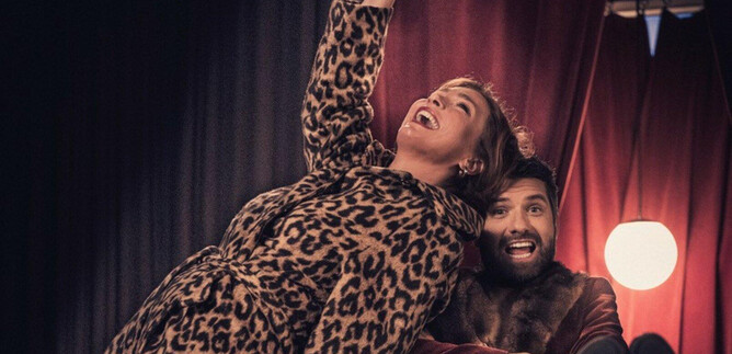 Two happy people are posing in a stylish room. The woman is wearing a leopard coat and seems to be having fun, while the man is smiling relaxed. | © Salzburger Kulturvereinigung