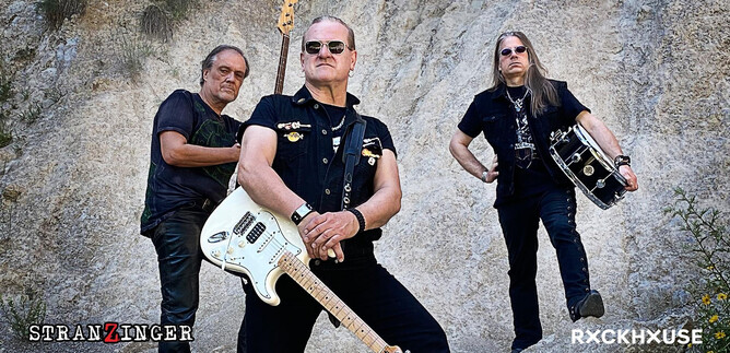 Drei Rockmusiker posieren vor einer Felswand. Einer hält eine Gitarre, während die anderen zwei Schlagzeug und Bass präsentieren. | © C.J. Price