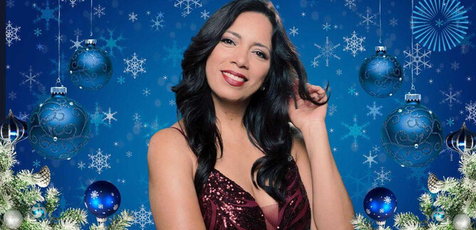 A woman with long, dark hair smiles in front of a blue, festive background. The background is decorated with snowflakes and Christmas ornaments. | © Amadeus Artists Vienna