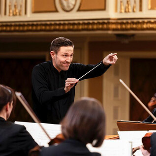 A conductor leads an orchestra in a festive hall. The musicians are attentive and play their instruments. | © Mozarteumorchester Salzburg