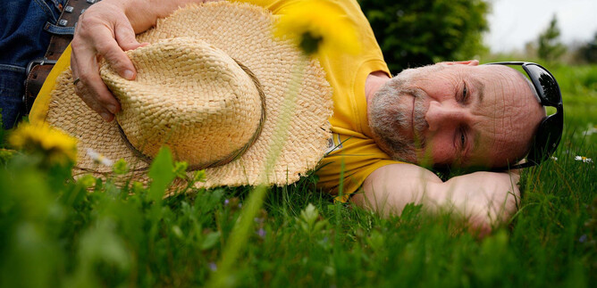 A man is lying relaxed on the grass wearing a sun hat. He enjoys nature in a quiet setting. | © Tom-Tom Lachmayr