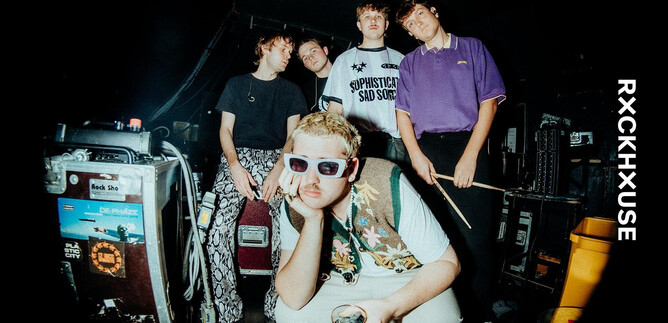 Eine Gruppe junger Leute posiert in einem Backstage-Bereich. Sie tragen auffällige Kleidung und Accessoires, während sie eine entspannte Atmosphäre ausstrahlen. | © Paul Strassner