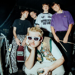 A group of young people is posing in a backstage area. They are wearing eye-catching clothing and accessories while emanating a relaxed atmosphere. | © Paul Strassner