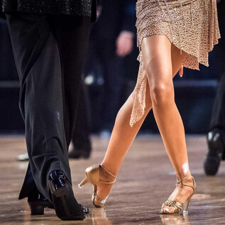 Táncosok, akik szenvedéllyel táncolnak egy táncparketten. Elegáns öltözékek és mozgó lábak mutatják a tánc dinamikáját. | © AdobeStock