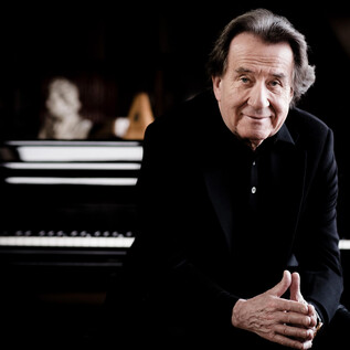 A smiling man sits in front of a piano. The background is dark and creates a creative atmosphere. | © Marco Borggreve