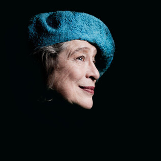 Une femme âgée avec un chapeau bleu sourit. L'image a un fond sombre et montre sa tête de profil. | © Marco Borggreve