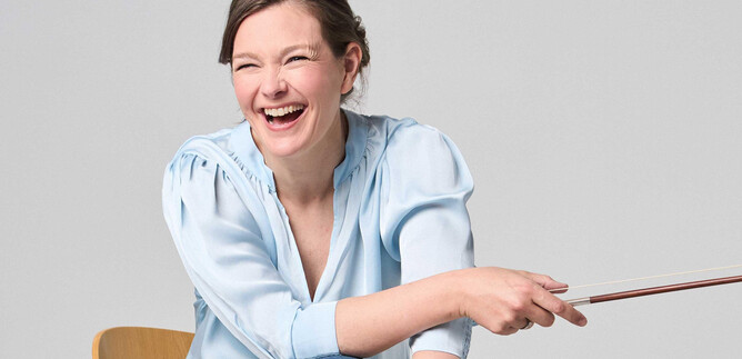 Eine lächelnde Frau sitzt auf einem Stuhl und hält einen Zeigestock. Sie trägt ein hellblaues Hemd und wirkt fröhlich und begeistert. | © Kaupo Kikkas