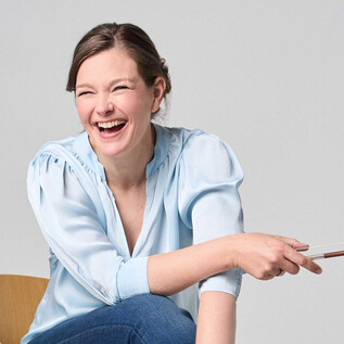 A smiling woman is sitting on a chair and holding a pointer. She is wearing a light blue shirt and appears happy and excited. | © Kaupo Kikkas