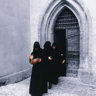 Four people in black robes stand in front of an old door. They seem to be engaged in a ceremonial act. | © Salzburger Virgilschola