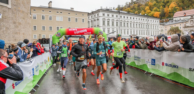 Eine Laufveranstaltung mit mehreren Teilnehmern, die unter einem bunten Startbogen loslaufen. Die Zuschauer stehen an der Seite und beobachten das Ereignis. | © Sportograf