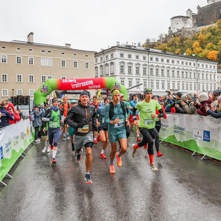 Un evento de carrera con varios participantes que salen corriendo bajo un arco de inicio colorido. Los espectadores están a un lado y observan el acontecimiento. | © Sportograf
