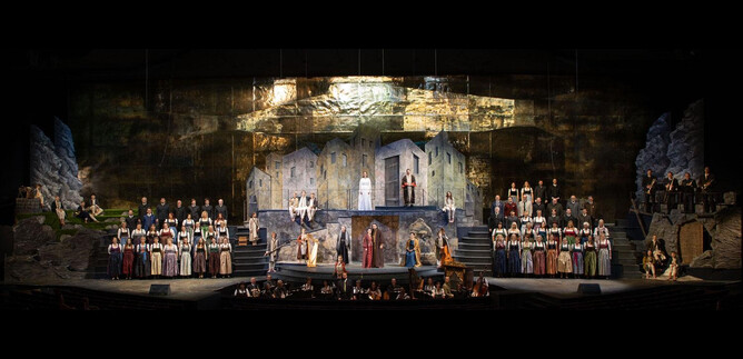 An impressive theater performance featuring many actors in historical costumes. The backdrop displays a dramatic landscape with rocks and buildings. | © Franz Neumayr