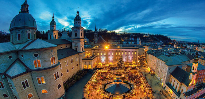 A picturesque city view at dusk with illuminated buildings and a festive Christmas market in the center. The atmosphere is cozy and inviting. | © Tourismus Salzburg GmbH