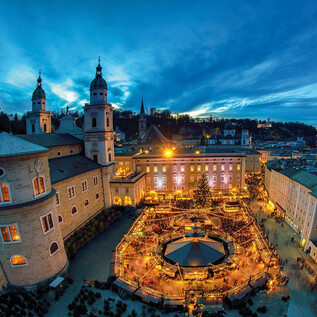 Eine malerische Stadtansicht bei Dämmerung mit beleuchteten Gebäuden und einem festlichen Weihnachtsmarkt im Zentrum. Die Atmosphäre ist gemütlich und einladend. | © Tourismus Salzburg GmbH