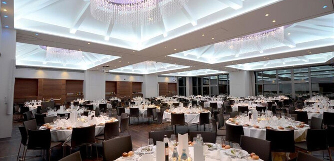 An elegant dining room with festively laid tables. The ceiling is brightly illuminated and the room radiates a luxurious atmosphere. | © Imlauer Hotel Pitter