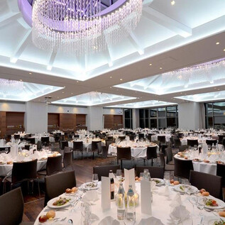 An elegant dining room with festively laid tables. The ceiling is brightly illuminated and the room radiates a luxurious atmosphere. | © Imlauer Hotel Pitter