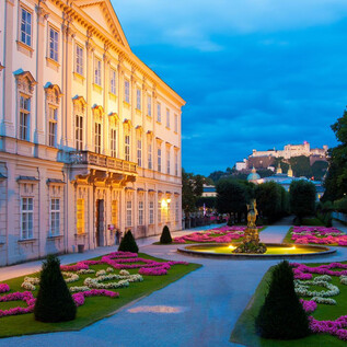 Ein wunderschöner Garten mit bunten Blumen und gepflegten Rasenflächen. Im Hintergrund ist ein historisches Gebäude und eine Burg zu sehen. | © Salzburger Konzertgesellschaft