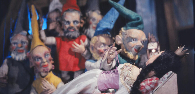A group of colorful dolls stands around a sleeping figure. The scene looks fairy-tale-like and inviting. | © Salzburger Marionettentheater