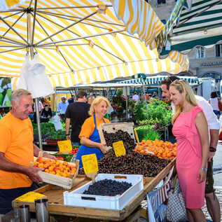 Targ pełen życia z świeżymi owocami i przyjaznymi sprzedawcami. Ludzie cieszą się atmosferą i wybierają z różnorodnej gamy produktów. | © Tourismus Salzburg GmbH, Breitegger G.