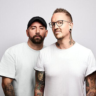 Deux hommes se tiennent côte à côte et regardent la caméra. Tous deux ont des tatouages visibles et portent des vêtements décontractés. | © Barracuda Music GmbH