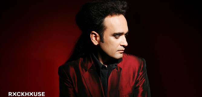 A man with dark, voluminous hair is wearing a red suit. The background is in a vibrant red. | © Rockhouse Salzburg